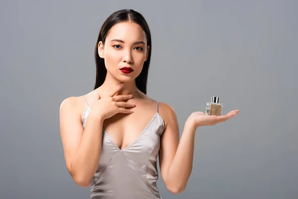 Elegante asiático mujer en elegante vestido con rojo labios celebración perfume aislado en gris — Stock Photo