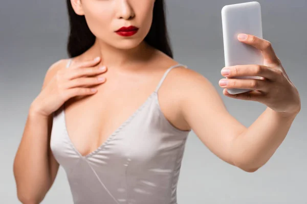 Cropped view of beautiful woman in satin dress with red lips taking selfie isolated on grey — Stock Photo