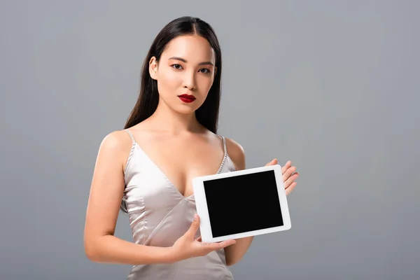 Belle femme asiatique en robe de satin avec lèvres rouges tenant tablette numérique avec écran vide isolé sur gris — Photo de stock