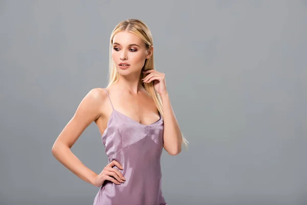 Élégante fille blonde en robe de satin violet regardant vers le bas avec la main sur la hanche isolé sur gris — Photo de stock