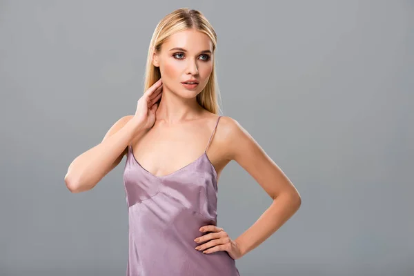 Элегантная блондинка в фиолетовом атласном платье позирует изолированно на сером — стоковое фото