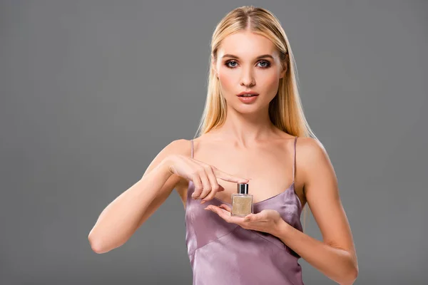 Elegant blonde woman in satin violet dress holding perfume isolated on grey — Stock Photo