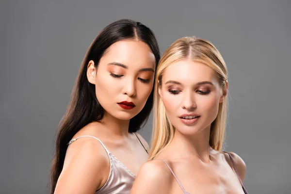Elegant blonde and brunette women in satin dresses looking down isolated on grey — Stock Photo