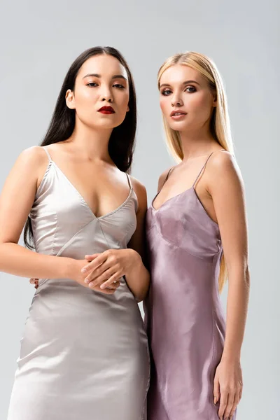 Low angle view of elegant blonde and brunette women in satin dresses isolated on grey — Stock Photo
