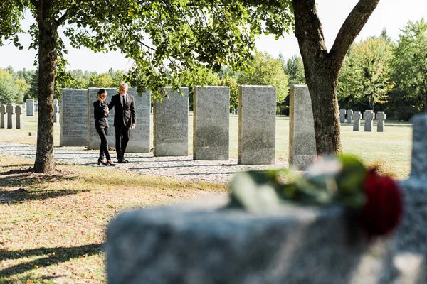 Selective focus of man and woman walking near tombstones — Stock Photo