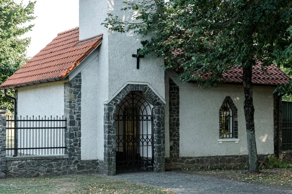 Alberi vicino alla chiesa cristiana con tetto rosso e recinzione metallica — Foto stock