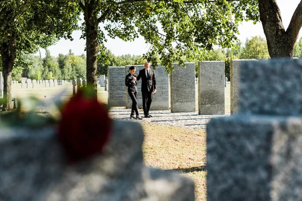 Selective focus of man and woman walking near tombstones in cemetery — Stock Photo
