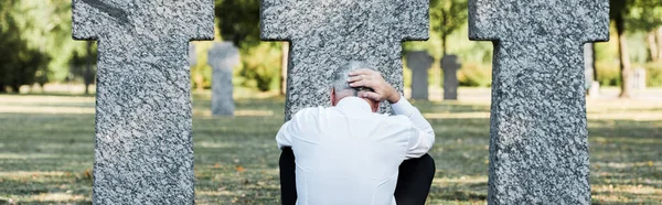 Tiro panorâmico de homem sênior sentado perto de túmulos — Fotografia de Stock