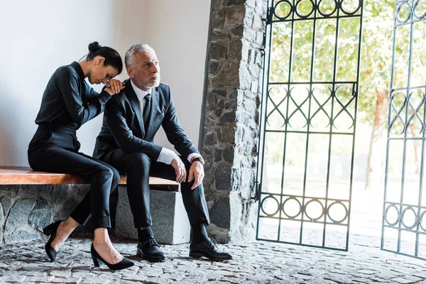 Triste donna seduta vicino turbato anziano uomo nel cimitero — Foto stock