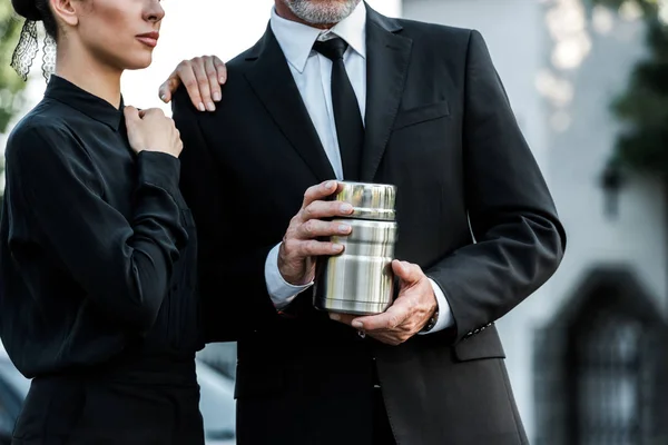 Cropped view of woman standing near bearded man holding cemetery urn — Stock Photo