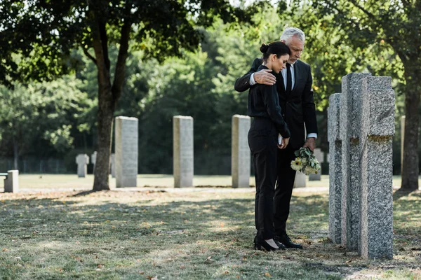 Upset man hugging frustrated woman in cemetery — Stock Photo