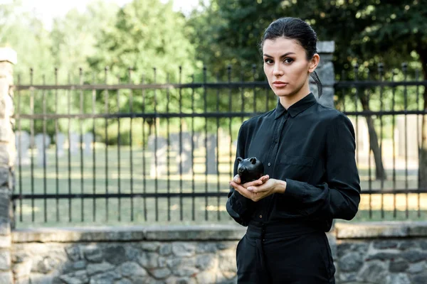 Attractive woman holding black piggy bank near metallic fence — Stock Photo