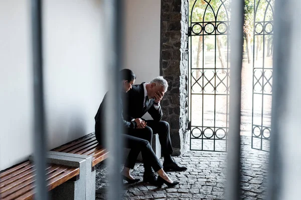 Красивая женщина сидит на скамейке рядом с грустным старшим мужчиной на кладбище — стоковое фото