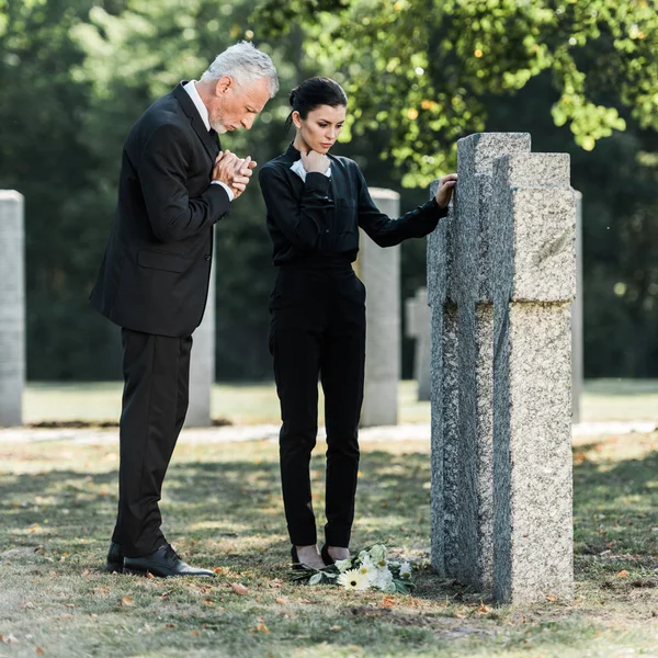 Uomo sconvolto con i capelli grigi e donna attraente in piedi vicino alle tombe — Foto stock