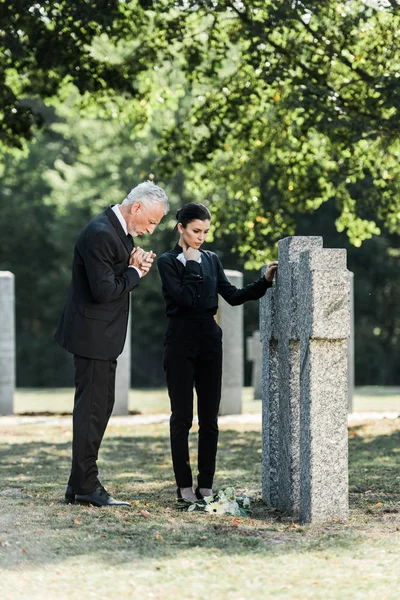 Upset man with grey hair and attractive woman standing near tombstones — Stock Photo