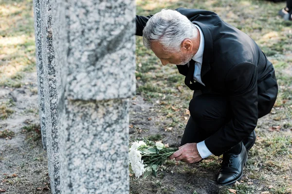 Selective focus of senior man putting white flowers near tomb — Stock Photo