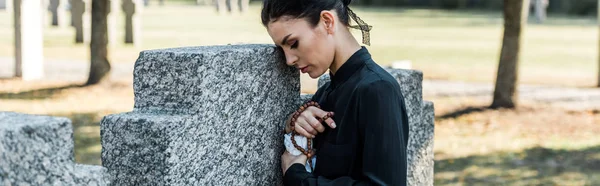 Colpo panoramico di donna triste che tiene rosario perline vicino alle tombe — Foto stock