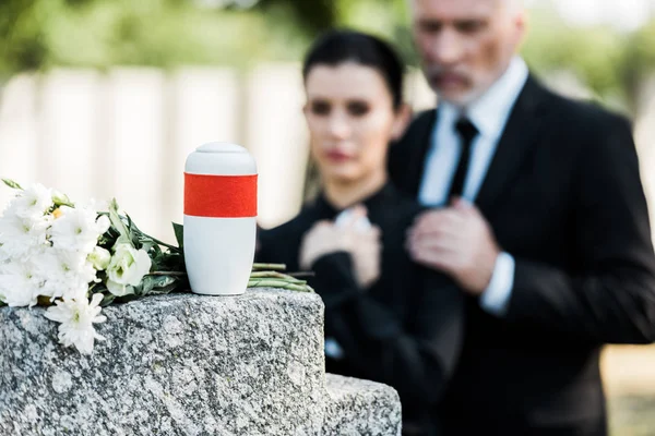 Selective focus of white flowers near mortuary urn and two people — Stock Photo