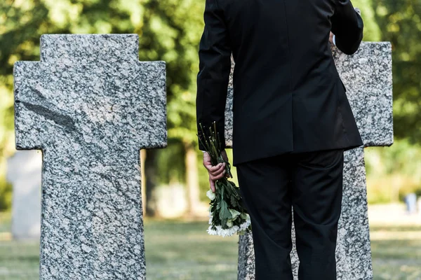 Vue recadrée de l'homme âgé debout près des tombes avec des fleurs — Photo de stock