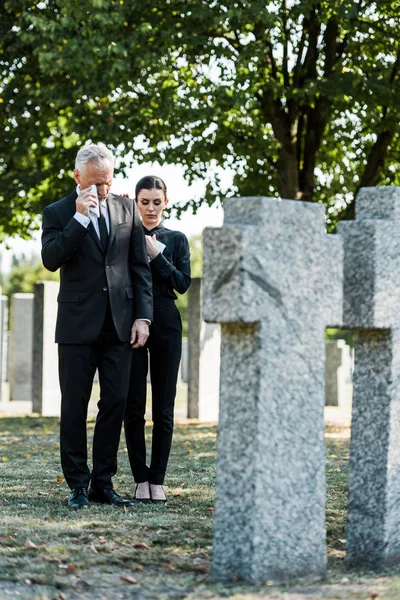 Hombre molesto llorando cerca de la mujer y lápidas en el cementerio - foto de stock