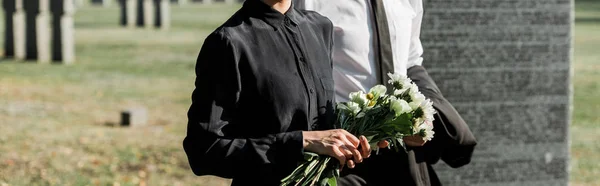 Panoramic shot of senior man near woman with flowers on funeral — Stock Photo