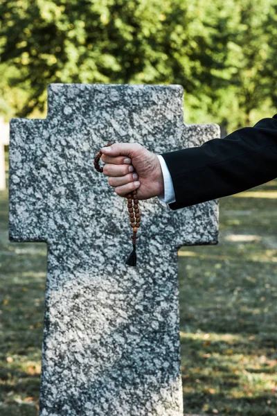 Vue recadrée d'un homme âgé tenant des perles de chapelet près de la pierre tombale — Photo de stock