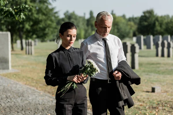 Bearded senior man walking near woman with flowers on funeral — Stock Photo