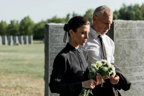 Uomo anziano barbuto vicino alla donna con fiori al funerale — Foto stock