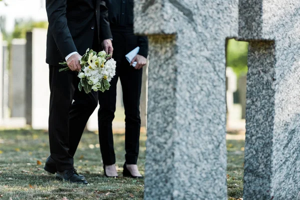 Abgeschnittene Ansicht eines Mannes, der neben einer Frau steht, mit Blumen in der Nähe von Gräbern — Stockfoto