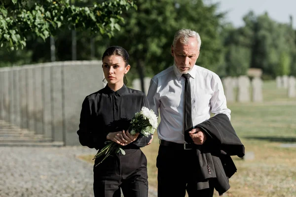 Handsome senior man standing with attractive woman holding flowers on funeral — Stock Photo