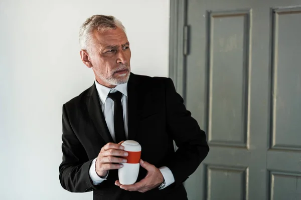 Upset bearded man in suit holding mortuary urn — Stock Photo