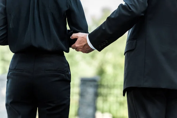 Vista recortada del hombre tocando la mano en la mujer de pie en el funeral - foto de stock