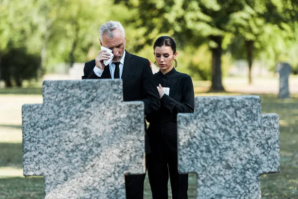 Enfoque selectivo de hombre molesto llorando cerca de la mujer en el funeral - foto de stock