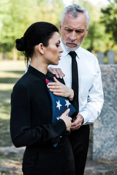 Селективное внимание бородатого мужчины, смотрящего на женщину с американским флагом на похоронах — стоковое фото