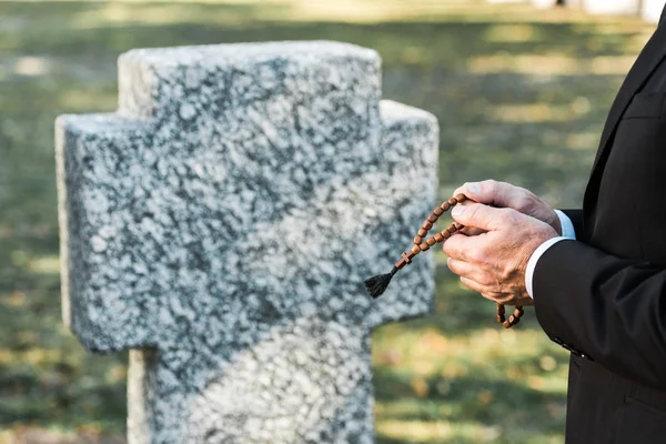 Обрезанный вид человека, держащего четки возле надгробия — стоковое фото