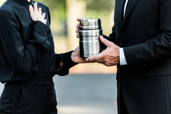 Cropped view of man and woman holding mortuary urn in graveyard — Stock Photo