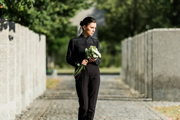 Mulher triste segurando flores brancas e andando no cemitério — Fotografia de Stock