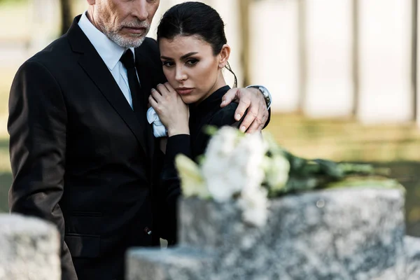 Selective focus of bearded man in suit hugging attractive woman in graveyard — Stock Photo