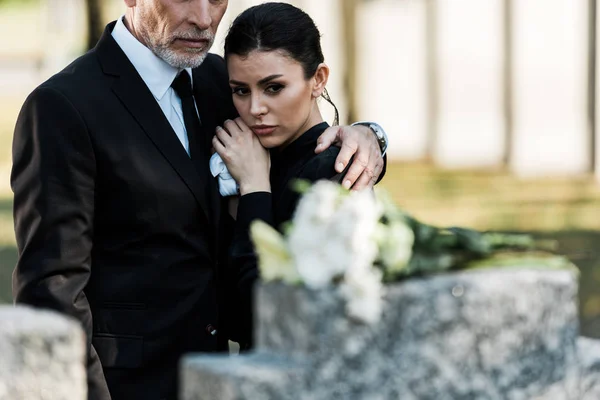 Foyer sélectif de l'homme barbu en costume étreignant femme attrayante dans le cimetière — Photo de stock