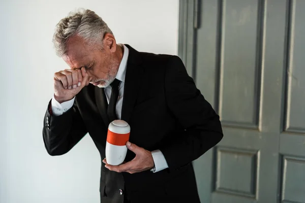 Sad bearded senior man crying while holding mortuary urn — Stock Photo