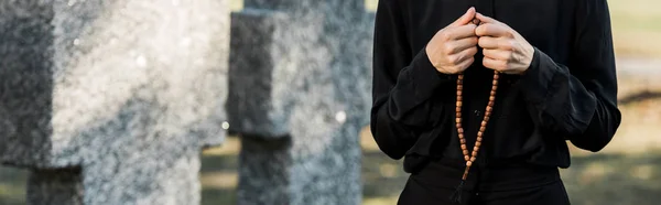 Panoramic shot of woman holding rosary beads near tombstones — Stock Photo