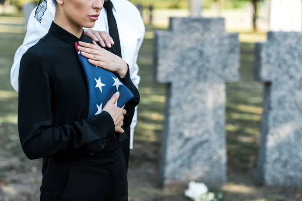 Обрезанный вид пожилого мужчины рядом с женщиной с американским флагом на похоронах — стоковое фото