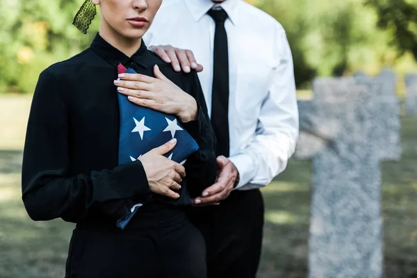 Обрезанный вид женщины с американским флагом рядом с мужчиной на похоронах — стоковое фото