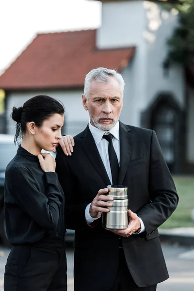 Upset woman standing near bearded senior man with mortuary urn — Stock Photo