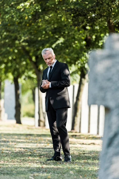 Selective focus of sad elderly man standing on graveyard — Stock Photo