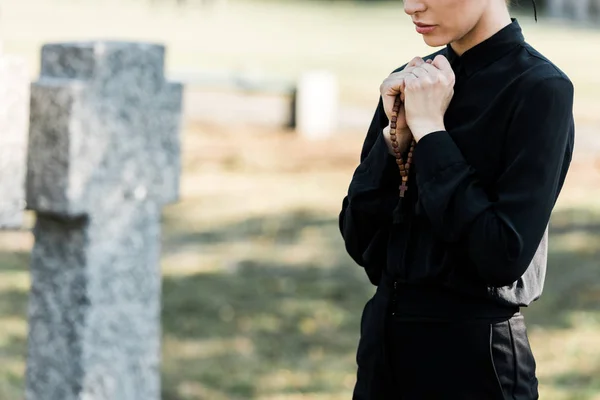 Cropped view of woman holding rosary beads near tombstone — Stock Photo