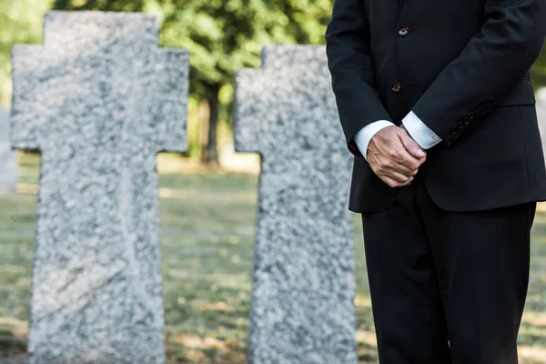 Ausgeschnittene Ansicht eines älteren Mannes, der mit geballten Händen in der Nähe von Gräbern steht — Stockfoto