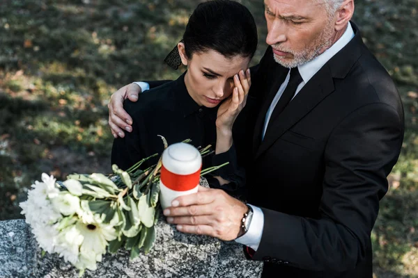 Overhead view of senior man hugging upset woman while holding mortuary urn — Stock Photo