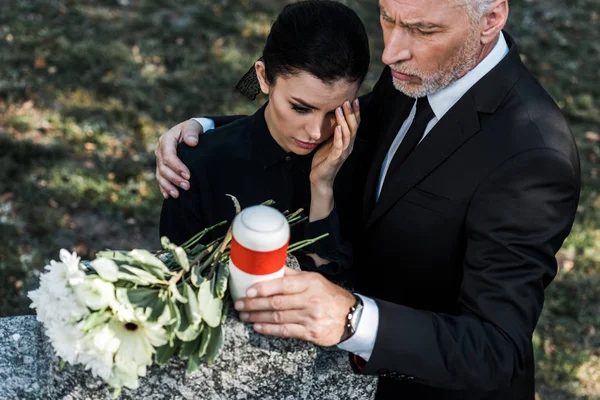 Vue aérienne de l'homme âgé étreignant femme bouleversée tout en tenant urne mortuaire — Photo de stock