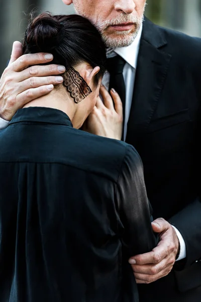 Recortado vista de mayor barbudo hombre abrazando mujer en funeral - foto de stock